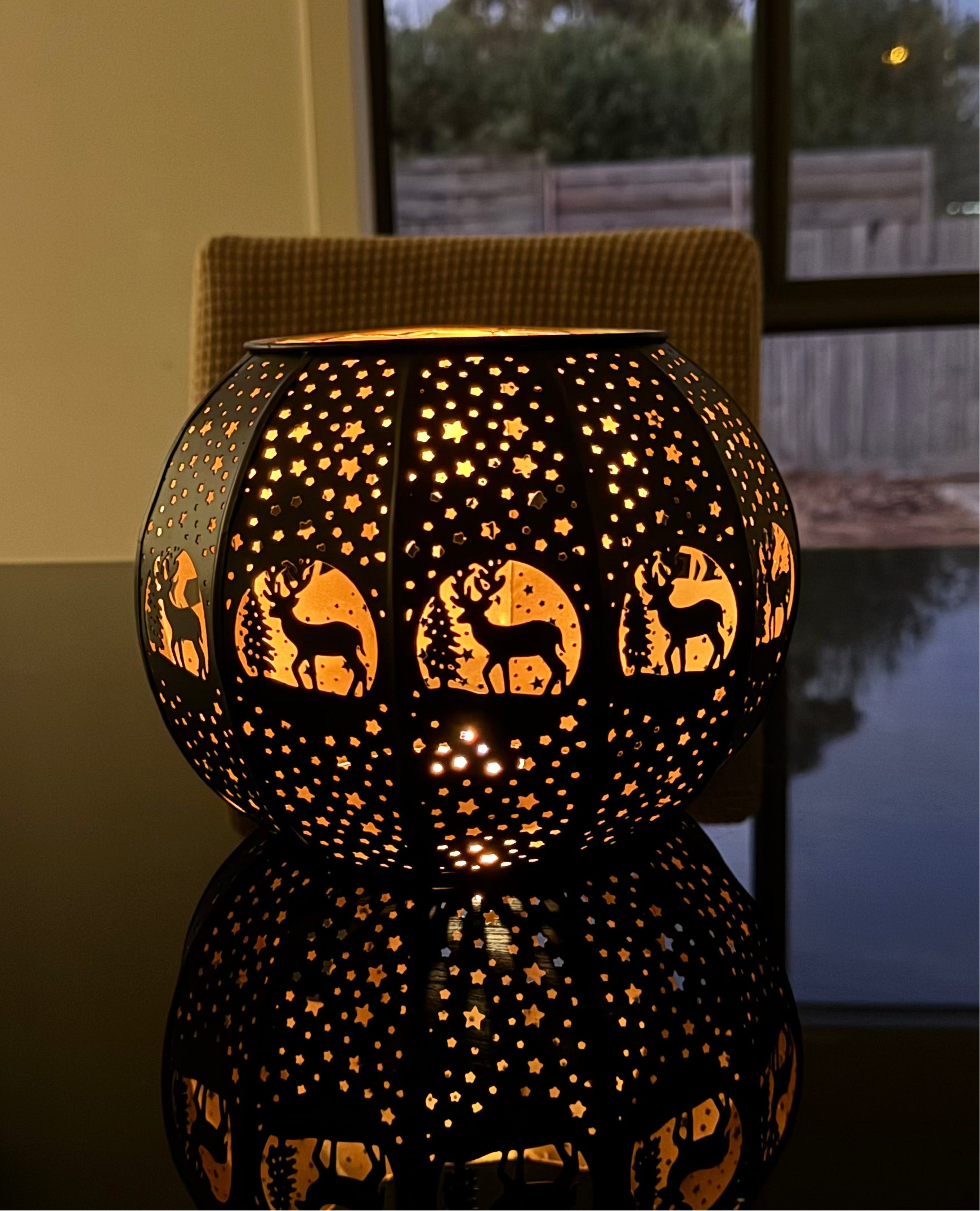 Brass candle lampswith intricate etchings, displaying a warm glow, placed on a surface near a window.