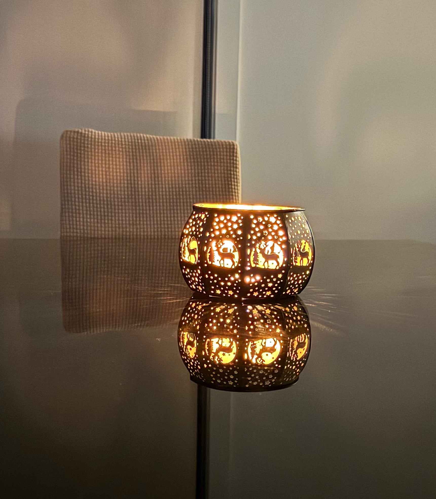 Three brass candle lamps with intricate etchings, displaying a warm glow, placed on a surface near a window.