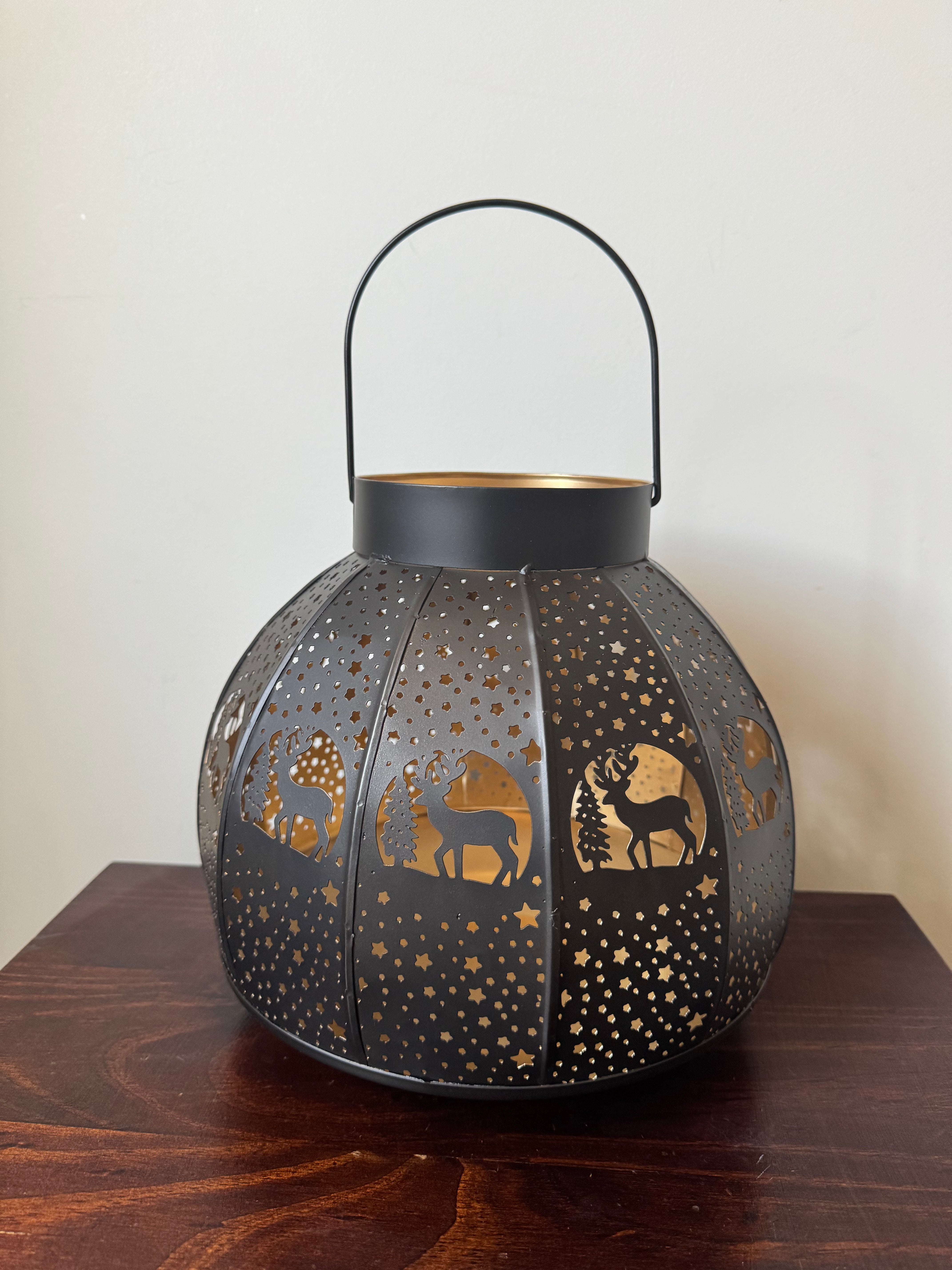 Large brass candle lamp with intricate etchings, displaying a warm glow, placed on a surface.